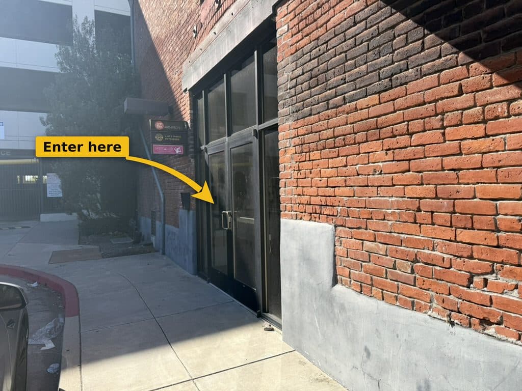 Black-framed glass double doors in a red brick wall, with a small sign post listing the building tenants to the left.