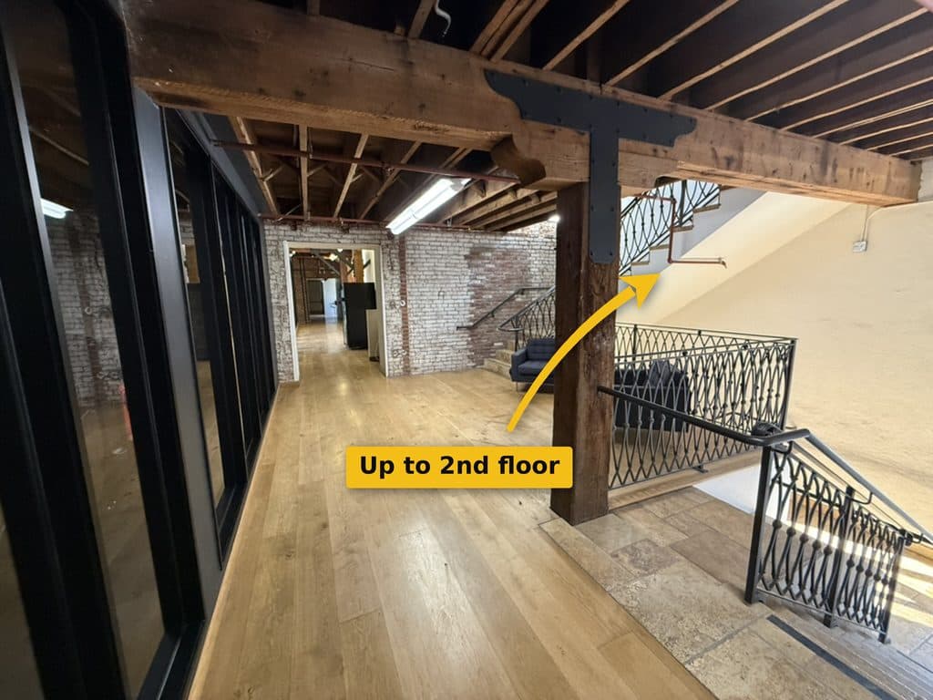 Landing with wood floors and exposed timber beams; a staircase with an iron railing goes up on the right.